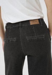 Črne kavbojke ravnega kroja, z dvema zadnjima žepoma in rjavim usnjenim oznako "CREAM" na pasu. Gladka tekstura.