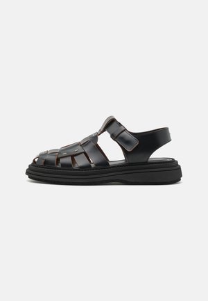 Schwarze Lederespadrilles mit einem geflochtenen Design, verstellbaren Riemen, metallischen Akzenten und einer dicken schwarzen Sohle für Stabilität.