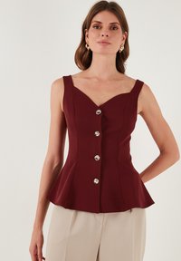 Bordo peplum top s V-izrezom, pet metalnih dugmadi i širokim naramenicama, izrađen od teksturirane tkanine.