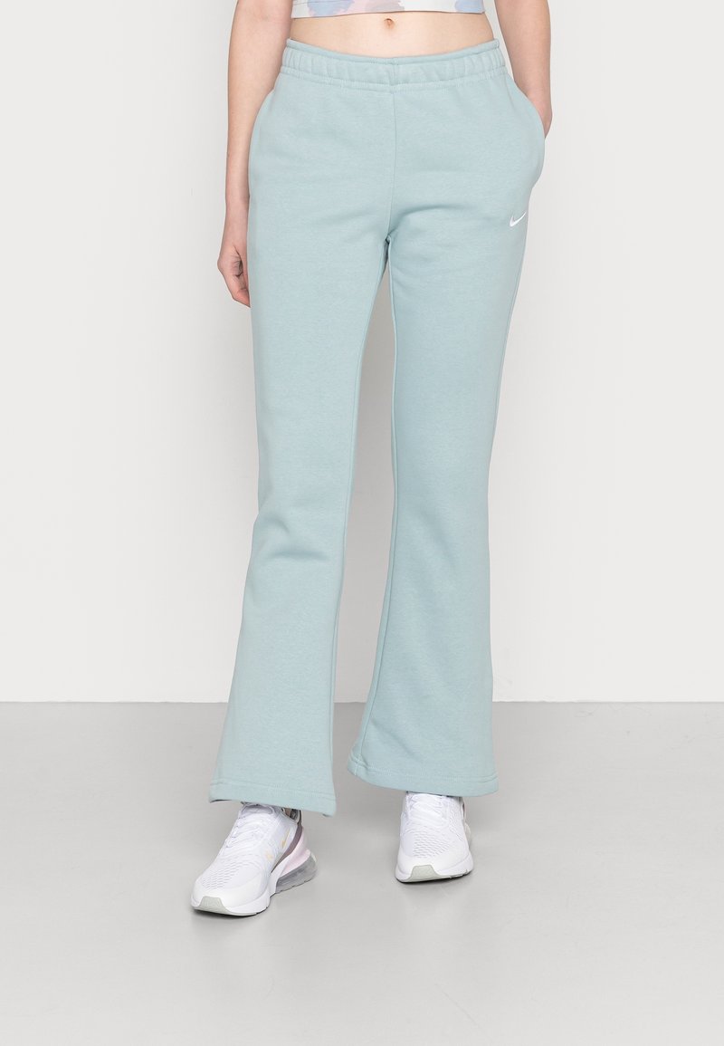 Světle modré, rozšířené tepláky vyrobené z měkké látky s elastickým pasem; na přední straně je malé bílé logo Nike.