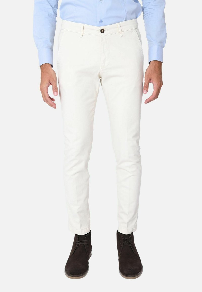 Pantaloni in cotone bianco misto con vestibilità slim, dotati di zip frontale, chiusura con bottone e tasche laterali, abbinati a stivali scuri.