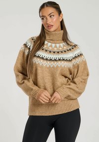 Turtlenecktröja i ljust brunt mao med ribbstickade ärmar och nederkant. Har ett geometriskt mönster i svart och ljusblått vid kragen.