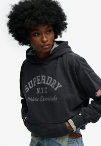 Ciemnoszara bluza z kapturem z dużym napisem "SUPERDRY", posiadająca przednią kieszeń, ściągacze na rękawach oraz naszywkę z amerykańską flagą na rękawie.