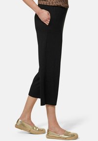 Pantalons cropped noirs avec une coupe décontractée et des poches latérales. Associés à des chaussures plates dorées brillantes et un haut à motifs. Texture de tissu lisse.