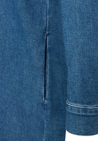 Blauwe denim stof met een gladde textuur, voorzien van een zijsplit, opgerolde manchetten en standaard stiksels. Het kledingstuk toont een strakke uitstraling.