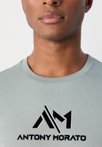 Grijze katoenen t-shirt met een zwart logo waarop de tekst "ANTONY MORATO" staat en geometrische designelementen aan de voorkant.