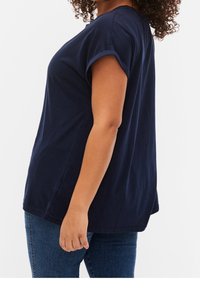 Marinblå bomulls T-shirt med korta uppvikta ärmar, avslappnad passform, rundad nederkant och mjuk textur, bärs med mörka denimjeans.