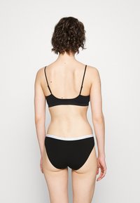 Fekete pamut bralette vékony pántokkal és egy hozzáillő fekete alsóval. A bralette deréknál egy fehér logózott elasztikus szalaggal van ellátva.