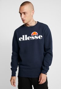 Tengerészkék pamutszövetről készült pulóver, nagy fehér "ellesse" logóval és egy színes félkör alakú díszítéssel a tetején. Rugalmas mandzsetták és alj.
