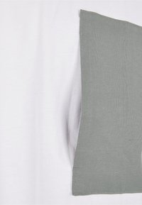 Hvit t-skjorte med en sydd grå lomme. Lommen har en glatt tekstur som kontrasterer med det myke stoffet i skjorten.