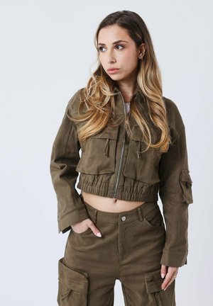 Chaqueta recortada verde oliva con cremallera frontal, dos bolsillos en el pecho y cintura elástica. Combinada con pantalones cargo a juego que cuentan con bolsillos laterales.