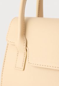 Μπεζ δερμάτινη τσάντα με δομημένο σχέδιο, που διαθέτει λεία επιφάνεια, κεντήματα και κοντή, στιβαρή χειρολαβή.