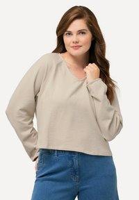 Beige langemouwshirt met een v-hals en raglanmouwen, met een relaxte pasvorm en een textuurstof. Gecombineerd met blauwe denim jeans.
