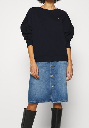 Felpa di cotone blu navy con maniche a palloncino, abbinata a una gonna in denim blu medio con bottoni davanti e una silhouette dritta.