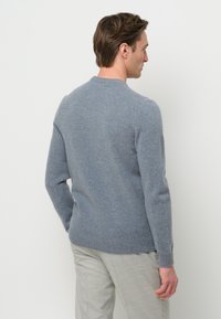 Grauer Strickpullover mit Rundhalsausschnitt, langen Ärmeln und passgenauem rippenstrick Abschluß. Die Textur wirkt weich und glatt, mit einem leicht melierten Muster.