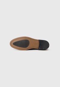 Semelle de chaussure en cuir noir avec un bord marron lisse. Présente un insert en caoutchouc texturé et des accents en métal doré près du talon.
