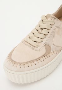 Baskets en suede beige avec une semelle épaisse blanche, bout rond, lacets ronds et couture décorative le long du bord supérieur.