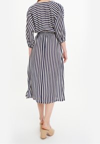 Marineblau-weißer gestreifter Midi-Kleid mit Dreiviertelärmeln, elastischem Bund und seitlichen Schlitzen, kombiniert mit hellen Keilsandalen.