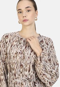 Vestido de manga larga y ligero en beige con patrones abstractos en marrón y verde. Cuenta con un escote fruncido y un cinturón de tela en la cintura.
