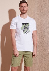 White crew-neck t-shirt featuring a graphic print in black and green, paired with olive green cargo shorts with side pockets and stitched details.