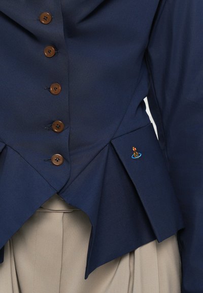 Navy blue tailored jacket with brown buttons, featuring a peplum design and an embroidered detail of a figure on the left side.