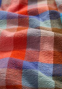Tessuto a quadri multicolore con superficie texture, caratterizzato da motivi arancioni, blu, rosa e marroni in varie tonalità e forme.