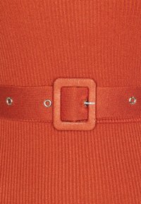 Tissu rouge côtelé avec une ceinture assortie dotée d'une boucle carrée et de ferrures en métal. La texture est lisse et légèrement extensible.