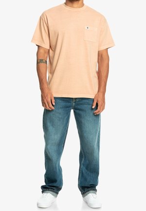 Hellpfirsichfarbene Baumwoll-T-Shirt mit kurzen Ärmeln und einer Brusttasche, kombiniert mit blauen Jeans und weißen Sneakers. Lässiger Schnitt und Design.