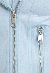 Světlomodrá bunda s dvojitými kovovými zipy, texturovanou látkou a svislými švy pro zvýraznění designu.