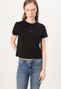 Tricou scurt negru, din bumbac, cu mâneci scurte și guler rotund. Logo-ul mic Calvin Klein centrat pe piept.