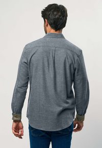 Szürke, hosszú ujjú gombos ing, lekerekített alsó résszel, kontrasztos zöld mandzsettával és hátrész díszítéssel. Az anyag lágy és textúrált hatású.