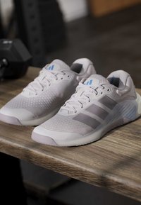 Ζευγάρι αθλητικά παπούτσια Adidas σε ανοιχτό γκρι με κορδόνια και τρεις πιο σκούρες γκρι ρίγες σε ξύλινη επιφάνεια.