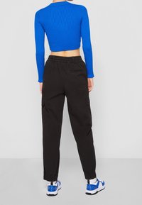 Modrý žebrovaný dlouhý rukáv crop top spojený s černými cargo kalhotami. Kalhoty mají elastický pas; boty jsou bílé s modrými akcenty.