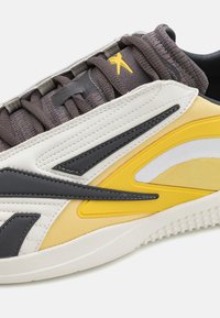 Sko med en grå, gul och vit syntetisk ovandel, texturerade meshdetaljer och en vit gummisula med ett upphöjt mönster.