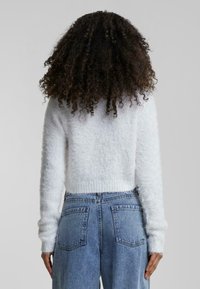 Pull en mohair blanc, court, avec manches longues, ourlet côtelé et surface texturée, associé à un jean en denim bleu clair taille haute.