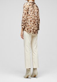 Blouse en soie beige doux à motif floral avec des manches trois-quarts, associée à un pantalon crème et des bottines à talons nus.