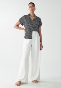 Zwart-wit gestreepte blouse met korte mouwen, gecombineerd met hoge witte wijde broek en platte sandalen, wat zorgt voor een strakke uitstraling.