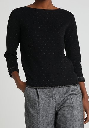 Pull noir à encolure bateau et manches trois-quarts, présentant un motif texturé de petits points argentés. Associé avec un pantalon gris.