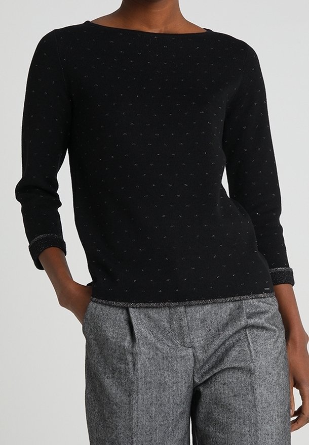 Maglione nero con scollo a barca e maniche a tre quarti, caratterizzato da un motivo testurizzato di piccole pois argentate. Abbinato a pantaloni grigi.