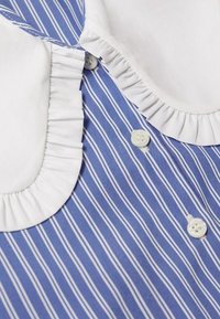 Chemise à rayures verticales bleues et blanches avec col à volants blanc et boutons blancs sur le devant.