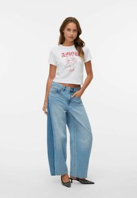 Hvid cropped t-shirt med rød "AMOR" print og tegneserie-grafik, parret med oversized lyseblå denim jeans, der har en afslappet pasform og lommer.