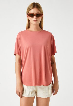 Rosa t-shirt med kort ärm och rund halsringning, gjord av mjukt tyg. Kombinerad med ljusa shorts för en avslappnad stil.
