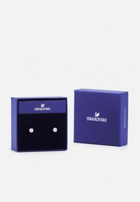 Swarovski crystal stud earrings displayed in a purple jewelry box, featuring black velvet padding and silver-tone hardware.