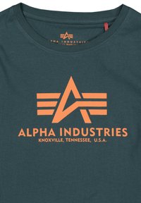 Tmavě modré bavlněné tričko s velkým oranžovým logem "Alpha Industries" a grafickým designem s textem, včetně informací o místě.