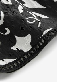 Tissu noir avec des motifs floraux blancs, présentant des détails en découpes le long de l'ourlet, et un bord texturé avec des ouvertures ovales.