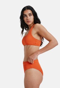 Top de bikini portocaliu cu nervuri, cu bretele late la umăr, asortat cu pantaloni scurți cu talie înaltă, tot din material cu nervuri. Textură netedă, design minimalist.