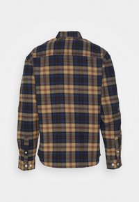 Camisa de franela a cuadros en azul marino, beige y óxido. Mangas largas con puños abotonados, detalle de canesú en la espalda y dobladillo redondeado. Textura suave.