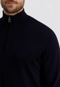 Marineblauwe zip-neksweater met een geribde kraag en textuurstof, met een ritssluiting van een kwart lengte en een aansluitende pasvorm. Minimalistisch ontwerp.