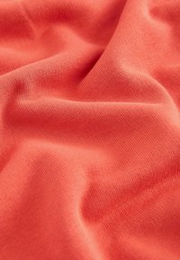 Tissu rose corail doux avec une texture en maille fine et de légers plis créant des ombres et des reflets subtils.