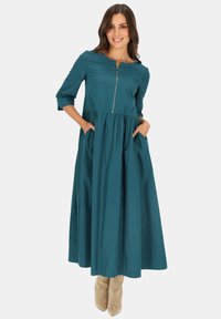 Turkusowa, średniej długości sukienka z okrągłym dekoltem, rękawami o długości trzech czwarte, zamkiem błyskawicznym z przodu oraz marszczonym dołem z dwiema kieszeniami.